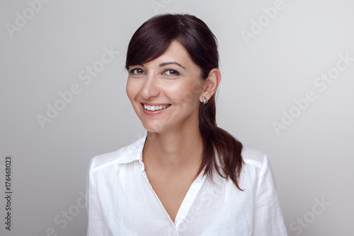 Closeup portrait of beautiful smiling young middle age brunette Caucasian woman with brown eyes looking in camera. Girl female with long dark hair in white office shirt. Studio beauty shot.
