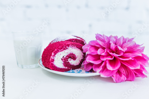 A red velvet cake roll sliced with cup of milk and flowers. photo