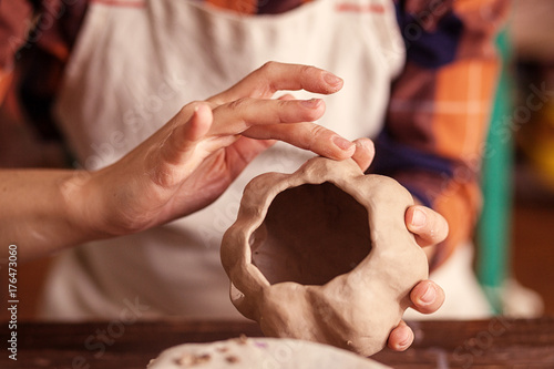 A close-up of a female potter sculpts a small pumpkin with clay jacka with a jack's face for Halloween on a wooden table background