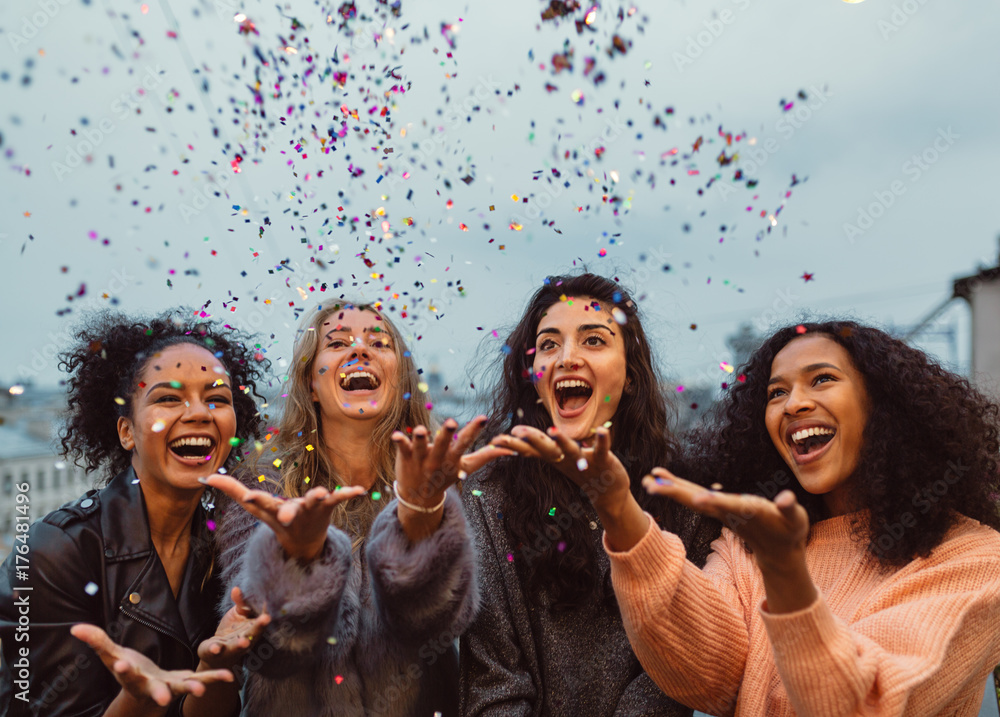 Happy friends standing on a terrace. Group of young women throwing confetti. - obrazy, fototapety, plakaty 
