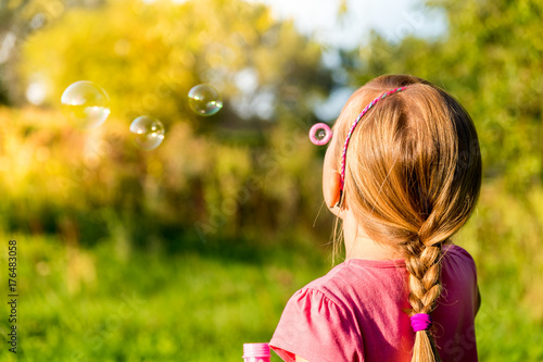 Beautiful young girl blowing soap bubbles in the summer park.