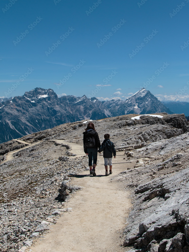 Mother and Son Walking in Stone Path among Barren Mountains in Italian Dolomites Alps in Summer Time