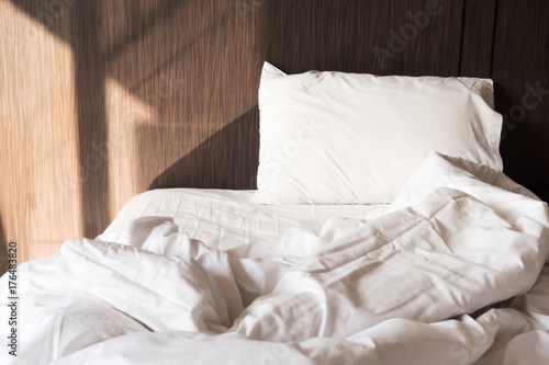 Messy bed. White pillow with blanket on bed unmade. Concept of relaxing after morning. With lighting window.