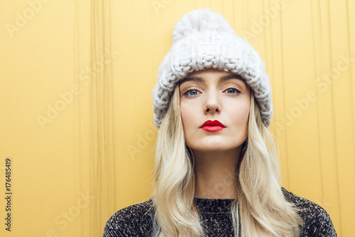 Portrait of a beautiful blonde woman wearing a large warm winter hat. Nice background of this composition is created of yellow wall.