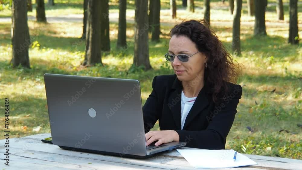 A girl in a business suit is working in nature. Business woman in park with laptop warm up. A girl in a business suit is working in nature. Business woman in park with laptop warm up.