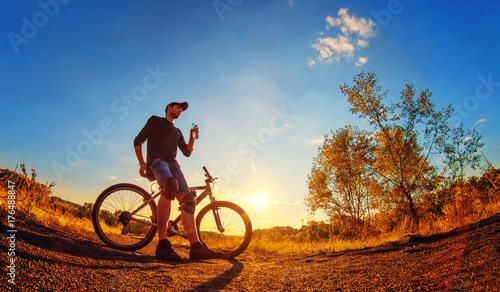 oung athletic guy in a black T-shirt, blue jeans shorts and knee pads on a sports bike © olegphotor