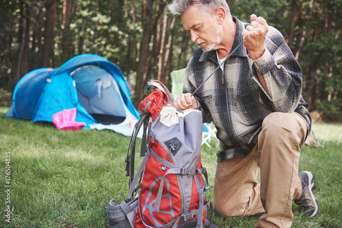 Senior man beside tent, packing rucksack photo