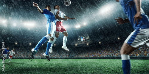 Soccer players performs an action play on a professional rainy stadium. Two football teams fighting for the ball. Players wears unbranded sport uniform. © Alex