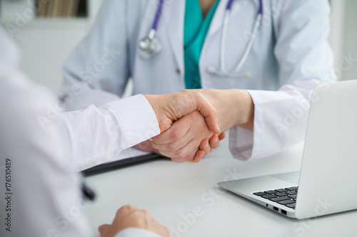 Doctor and patient shaking hands, close-up. Physician talking about medical examination results. Medicine, healthcare and trust concept