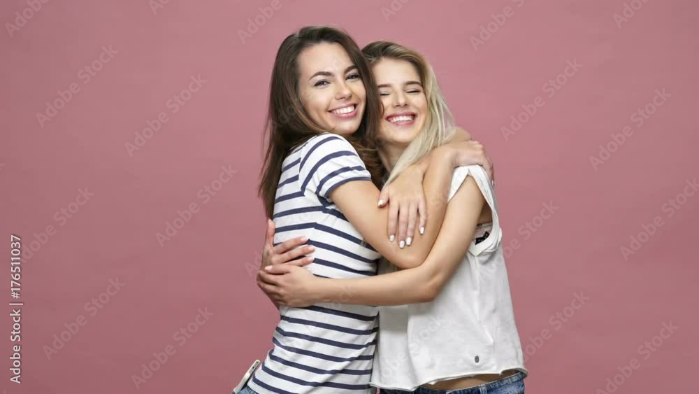 Pretty cheerful caucasian women friends in casual clothes hugging isolated over pink Pretty cheerful caucasian women friends in casual clothes hugging isolated over pink