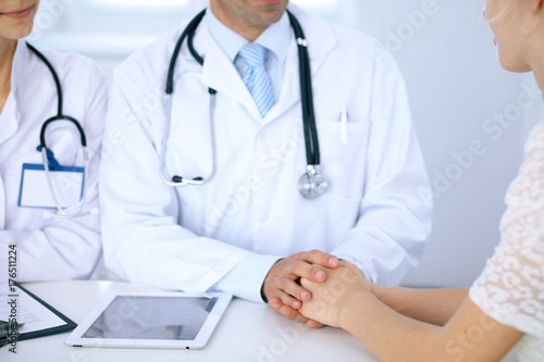 Fototapeta Naklejka Na Ścianę i Meble -  Doctor reassuring his female patient by touching her hands while talking. Symbol of support and trust in medicine
