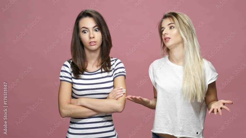 Young excited blonde woman talking to her bored brunette friend isolated over pink Young excited blonde woman talking to her bored brunette friend isolated over pink