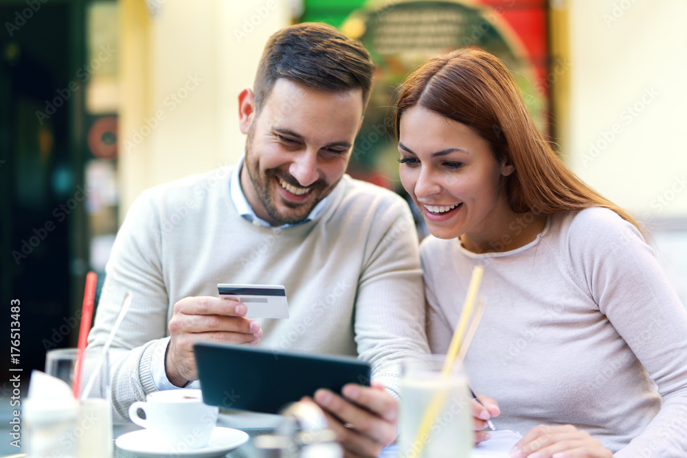 Beautiful young couple is doing shopping online using a digital tablet  smiling while resting in cafe