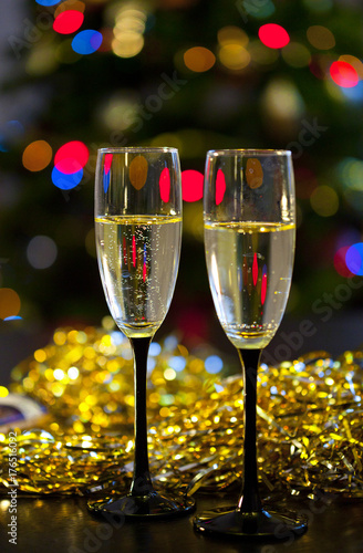 Новогодний натюрморт с прозрачными бокалами шампанского на черных ножках на фоне золотой мишуры и огоньков новогодней елки
