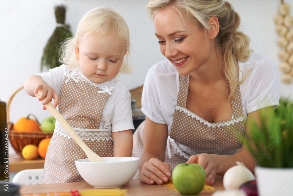 Mother and little daughter are cooking in the kitchen. Spending time all together or happy family concept Mother and little daughter are cooking in the kitchen. Spending time all together or happy family concept