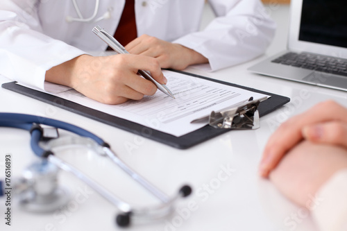 Close up of a female doctor filling up an application form while consulting patient