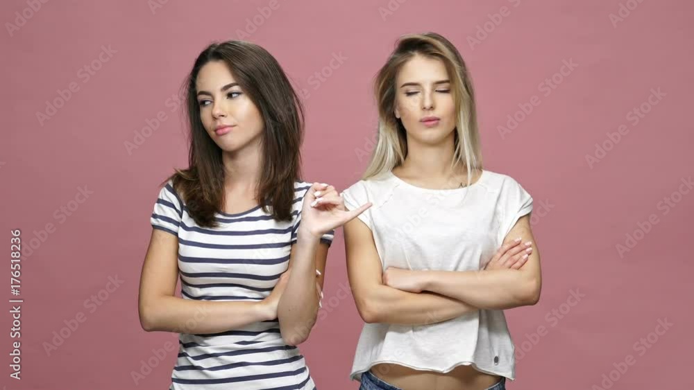 Two young beautiful offended ladies looking aside and making peace gesture isolated over pink Two young beautiful offended ladies looking aside and making peace gesture isolated over pink