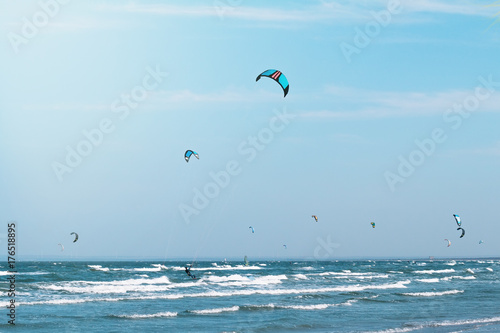 Kitesurfing in the wavy sea. Many kitesurfers on the sky background.