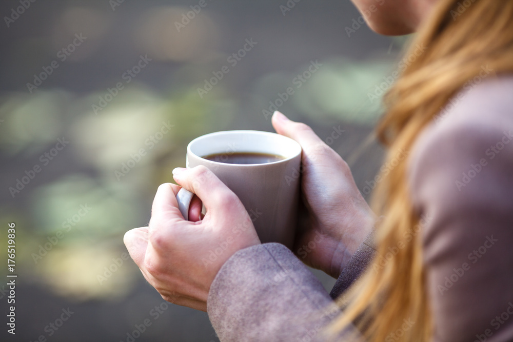 Closeup view of disposable cup of coffee or tea in womans hand. Autumn park with trees and yellow leafes Closeup view of disposable cup of coffee or tea in womans hand. Autumn park with trees and yellow leafes