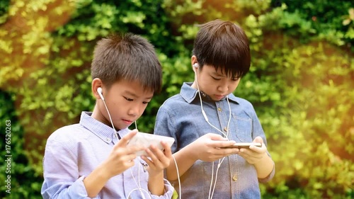 Slow motion of preteen Asian Thai boy is using smartphone to play game in his home garden. Technology and health concept photo