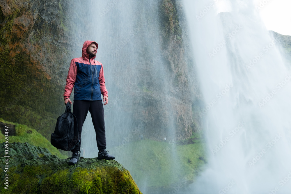 Fototapeta premium Adventure man by skogafoss waterfall, nature on Iceland. Young man visiting nature landscape.