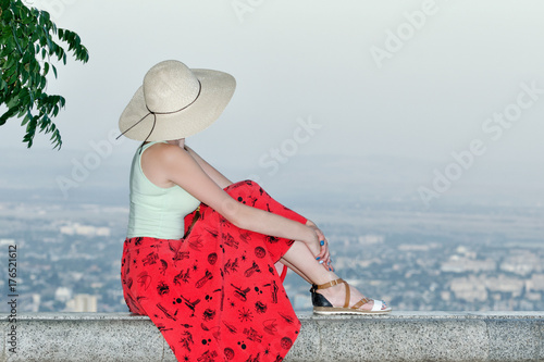 Girl in hat sits and looks at the city from a height. Side view, evening time photo