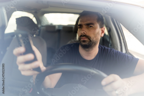 Man texting while driving.  Using a smartphone while driving.  Front view of man driving while using mobile phone.