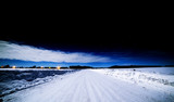 Black sky over the winter road. Snowy road and clouds illuminated by the Moon.