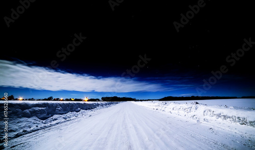 Black sky over the winter road. Snowy road and clouds illuminated by the Moon.