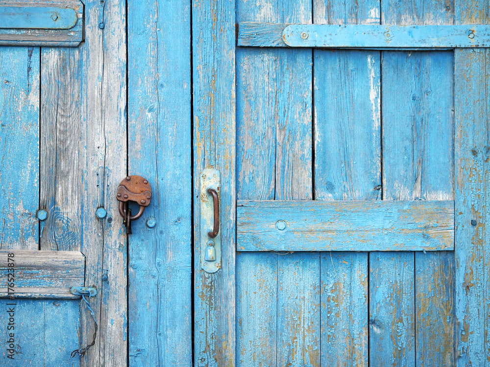 Ancient wooden gate closed on a rusty padlock, painted with old peeling light blue paint. Rural building background Ancient wooden gate closed on a rusty padlock, painted with old peeling light blue paint. Rural building background