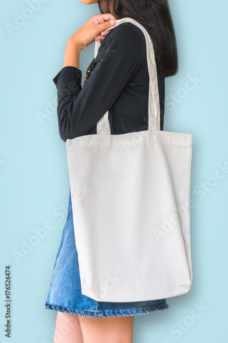 White tote bag mockup template cotton canvas fabric texture on girl shoulder (isolated with clipping path) on blue background