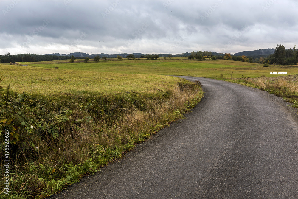 a narrow road leading between fields under storm clouds in autumn a narrow road leading between fields under storm clouds in autumn