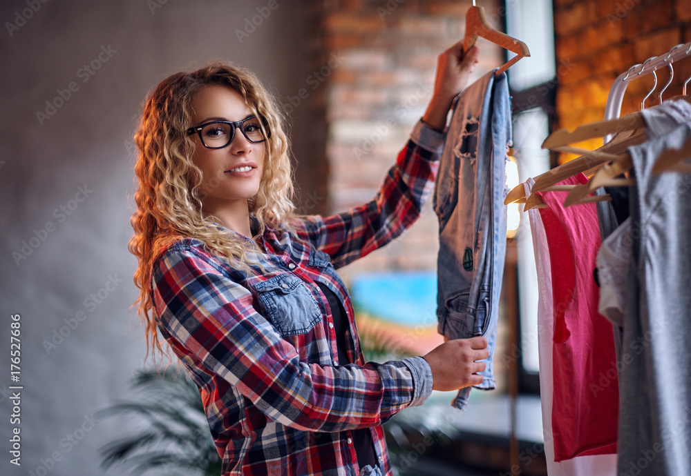Εκτύπωση καμβά A woman chooses fashionable clothes on the coat rack.