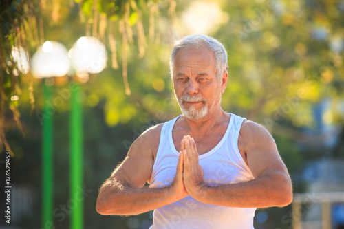 Grey Bearded Old Man in White Vest Shows Yoga Pose in Park