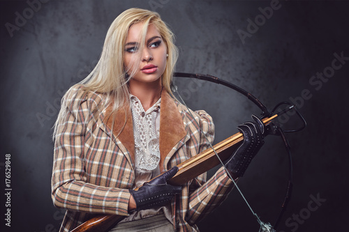 Studio portrait of blond old fashioned female holds a crossbow.