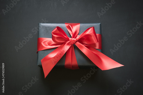 Gift box wrapped in black paper with red ribbon on black surface.