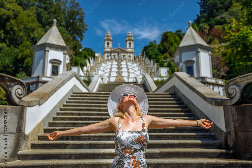 Freedom woman with open arms at beginning of baroque monumetal stairway to Bom Jesus do Monte Sanctuary. Female tourist enjoys at popular landmark and pilgrimage site, Braga, northern Portugal