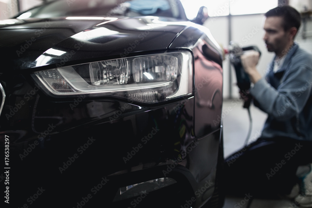 Fototapeta premium Car detailing - Hands with orbital polisher in auto repair shop. Selective focus.