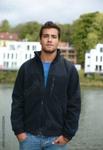 Foto junger Mann mit Jacke am Fluss vor Neubauten,Blick in die Weite oder ins Leere