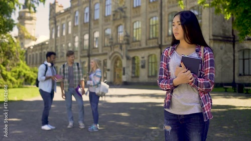 Lonely biracial girl standing alone, upset about mockery and jokes of classmates
