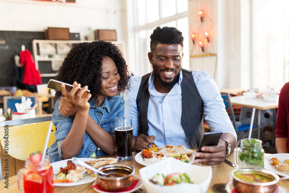 happy man and woman with smartphones at restaurant