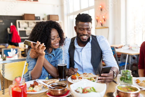 happy man and woman with smartphones at restaurant