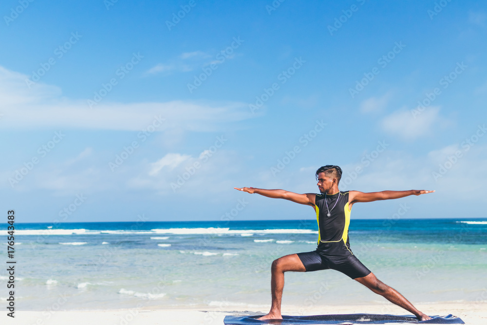 Obraz premium Asian yoga man practice yoga on the beach with a clear blue sky background. Yogi on the tropical beach of Bali island, Indonesia.