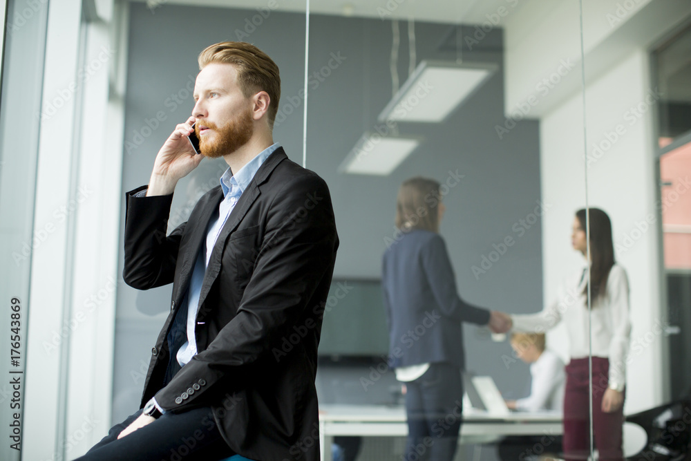 Businessman with ginger hair using mobile phone while other business people working in office Businessman with ginger hair using mobile phone while other business people working in office