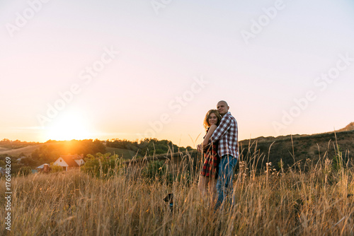 guy man in plaid shirt and girl in red checkered dress kiss standing in grass half top on sunset background