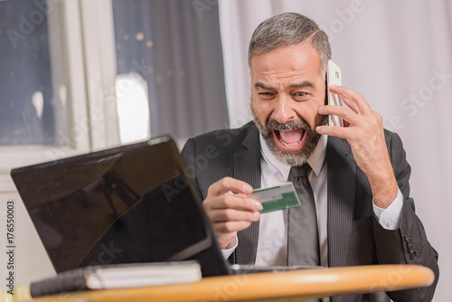 Shocked senior business arguing with the bank about his credit card balance, sitting in his office © Teodor Lazarev