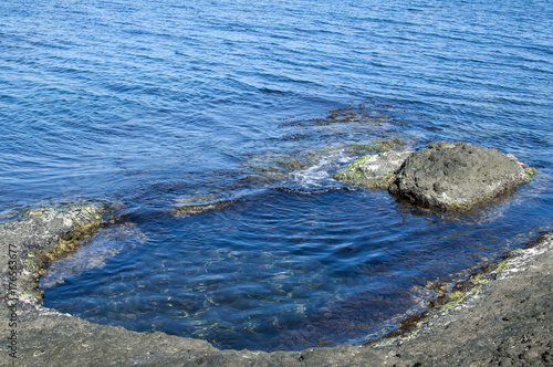 Small sea bay with blue clear calm waters among rocks in summertime as natural background