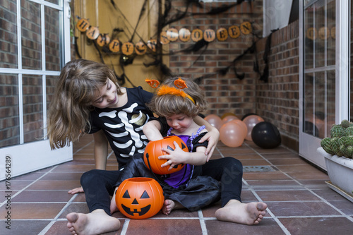 two happy little sisters having fun at home wearing halloween costumes and playing with pumpkins. Trick or treat. Indoors. Lifestyle
