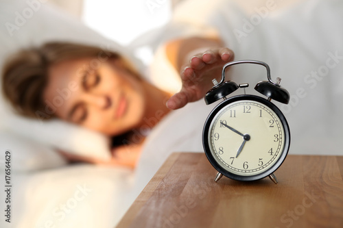 Photography Sleepy young woman stretching hand to ringing alarm willing turn it off