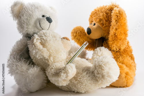 Three teddy bears, one has a medical thermometer on white background. © Svetlin